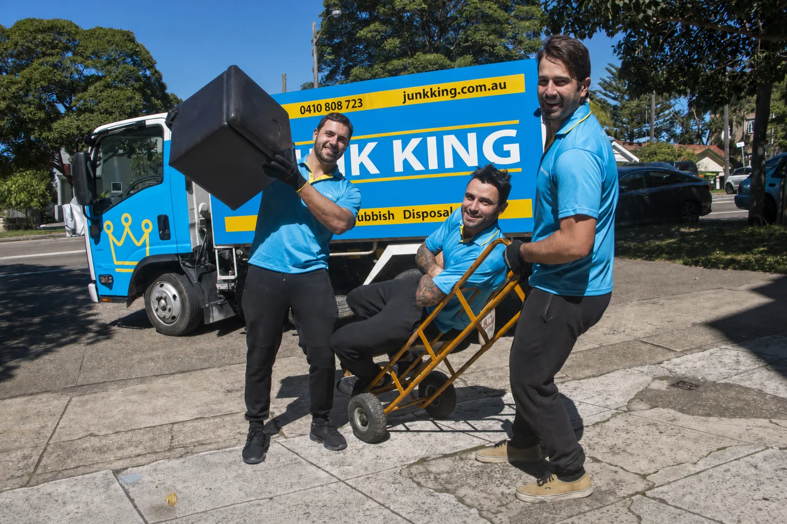 Junk King Sydney crew moving bulky furniture with a trolley beside the branded truck