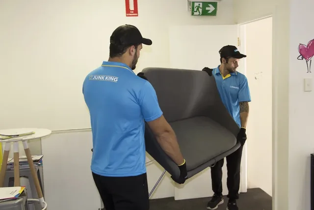 Junk King team carrying an unwanted sofa through a doorway